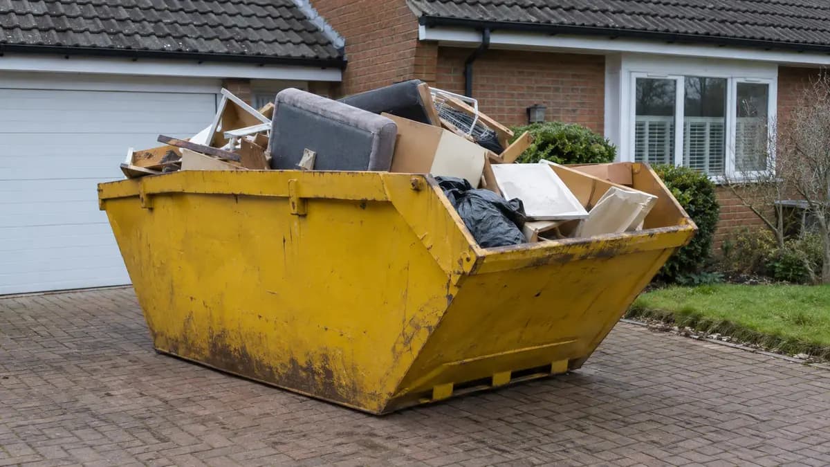 Benne de location remplie de mobilier sans tri, garée dans une allée
