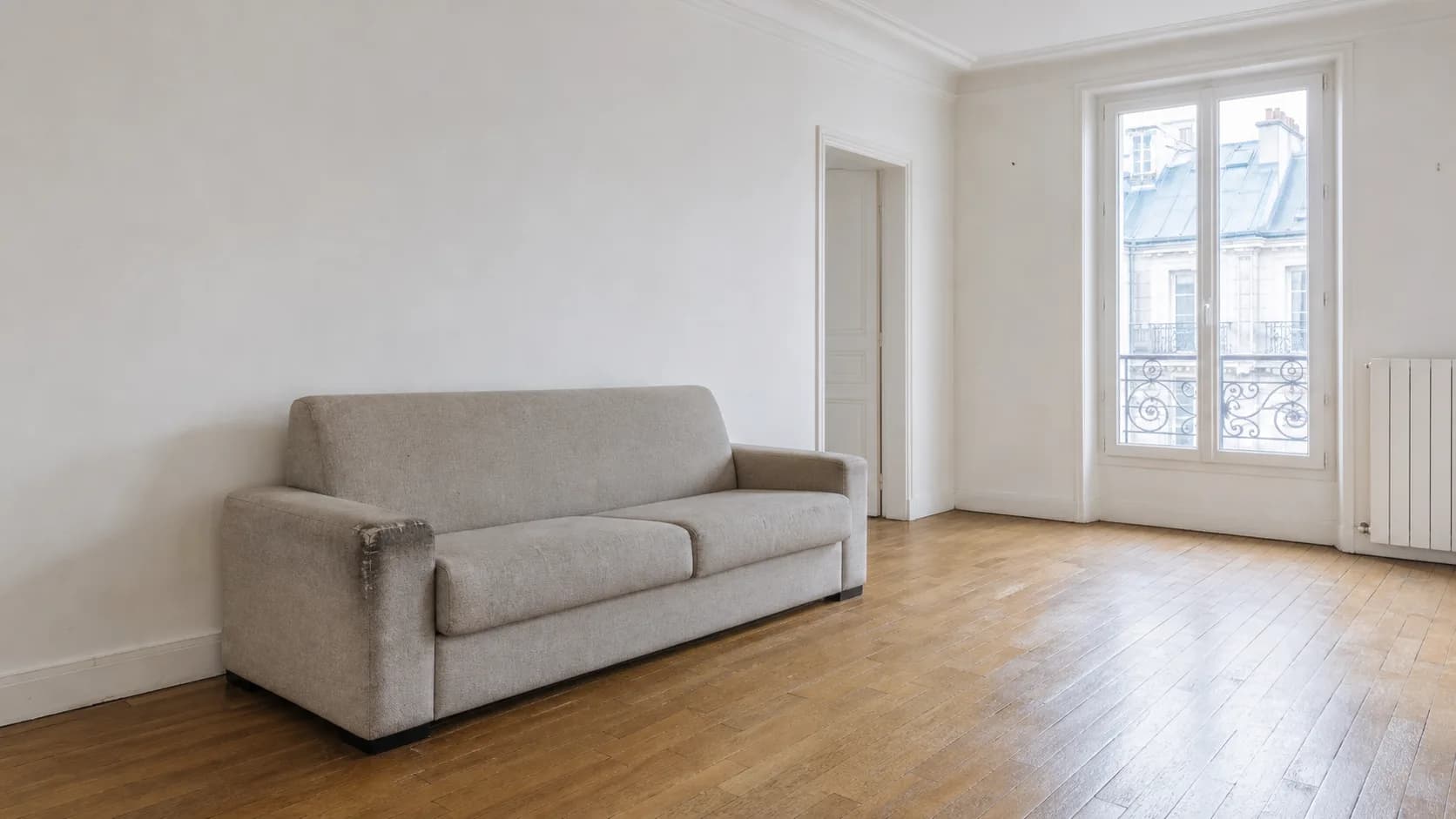 Canapé à l'accoudoir marqué par l'usage, dans un appartement vide avant l'état des lieux