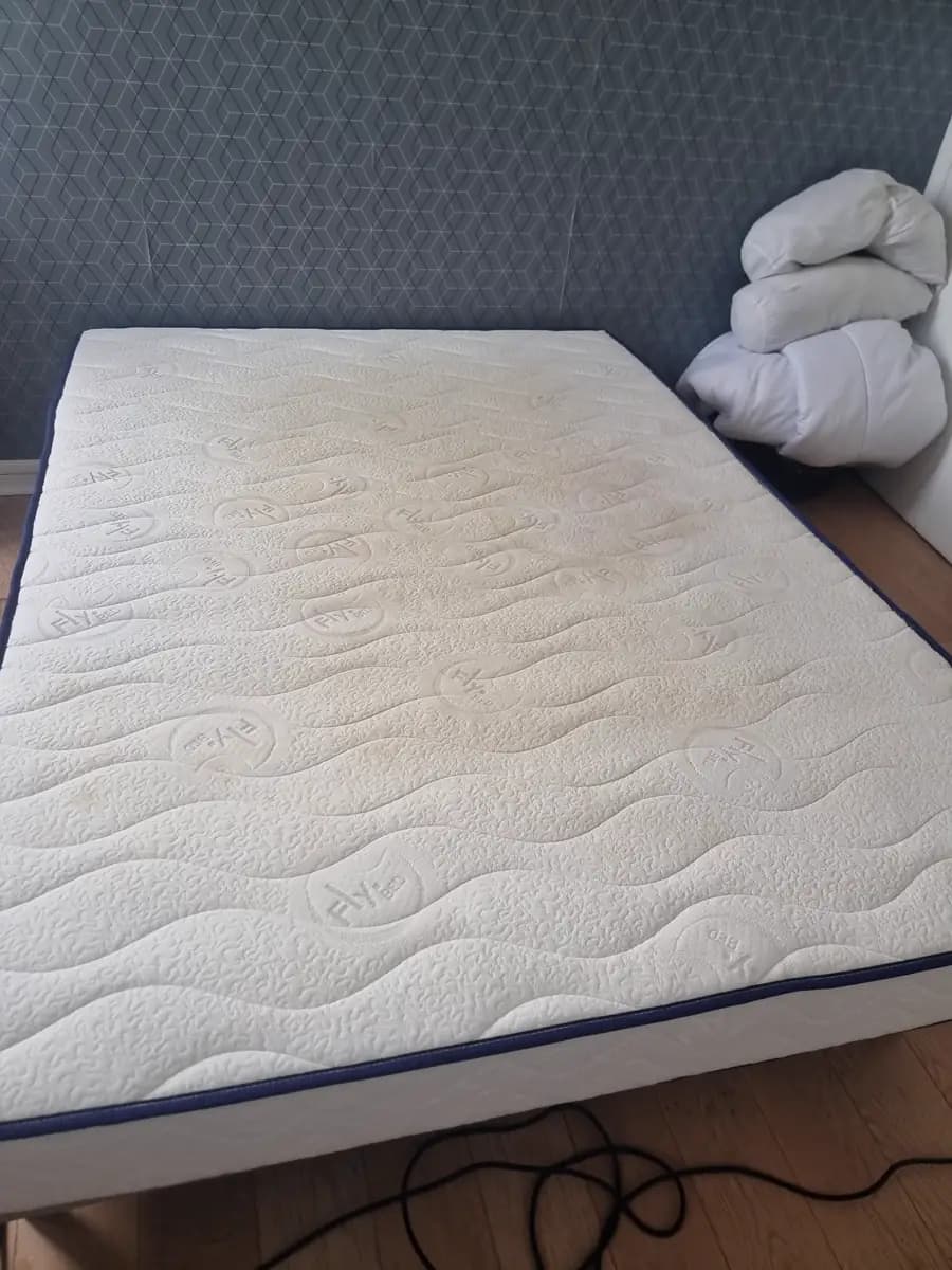 Matelas deux places posé sur son sommier, teinte jaunie au centre avant nettoyage