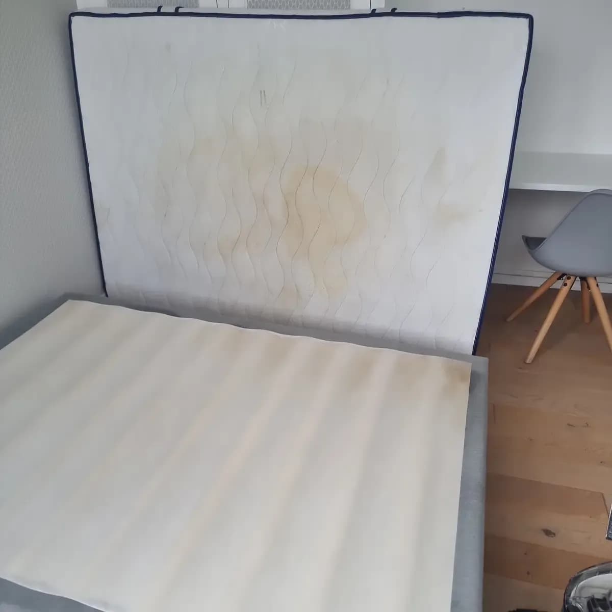 Matelas deux places auréolé de transpiration et son sommier dressés contre le lit, avant nettoyage